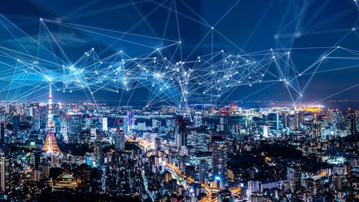 A cityscape at night with illuminated skyscrapers and digital network lines connecting various points.