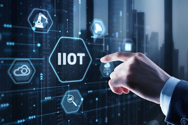 A hand points at a digital interface with hexagonal icons related to the industrial Internet of Things (IIoT) and IT and OT integration, set against a cityscape background.
