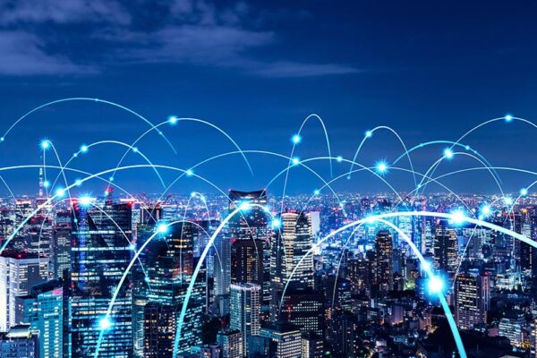 A city skyline at night with blue light trails and glowing points representing digital data or network connectivity across buildings.