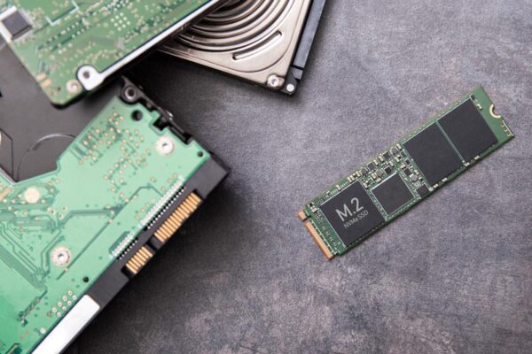 A hard drive and an SSD are stacked on the left, while a small form factor M.2 SSD lies separately on the right on a gray surface.