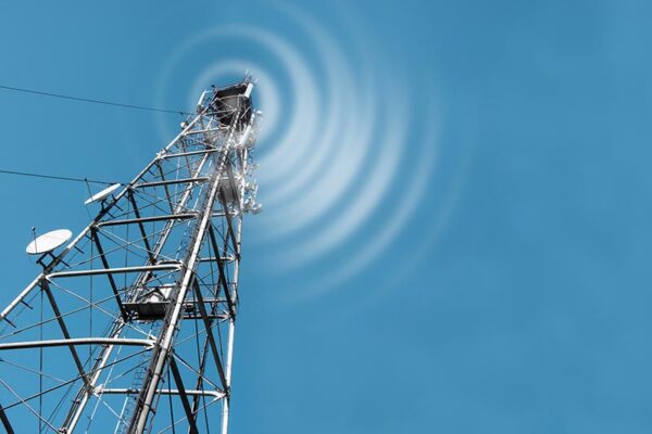 A metal telecommunications tower with antennas emits radio waves upward against a clear blue sky.