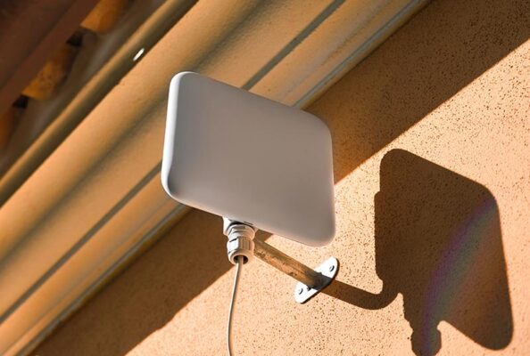 A white rectangular fixed wireless access antenna is mounted on an outdoor wall with an attached cable.
