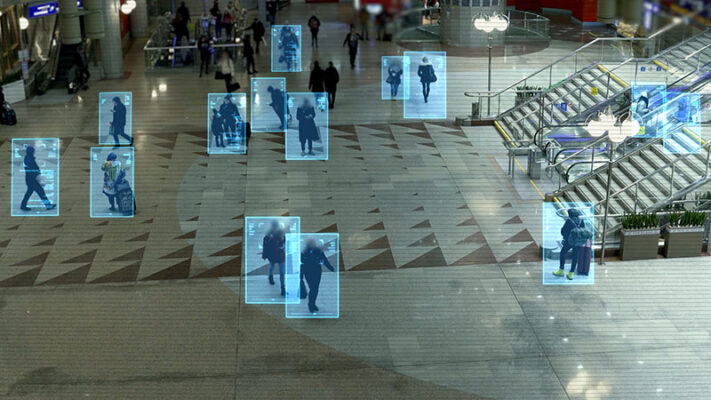 A crowd inside a building is visually tracked by rectangular digital overlays around people, capturing motion and locations.