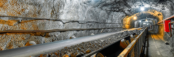 A conveyor belt carrying mined material runs through an illuminated underground tunnel with rocky walls and overhead piping, all monitored by a private 5G network.