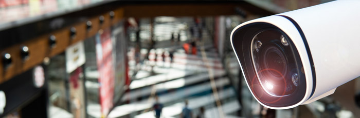 Close-up of a security camera, enhanced by private 5G, overlooking a multilevel shopping area with blurred figures in the background.