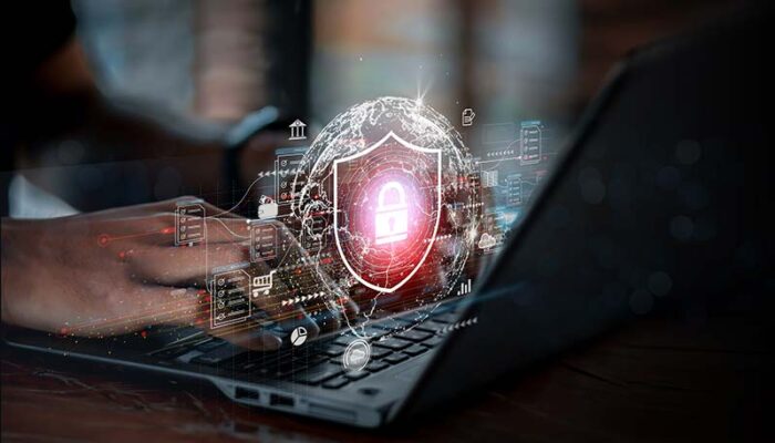 Hands typing on a laptop keyboard with a glowing padlock symbol overlaid, representing an end-to-end IoT security strategy.