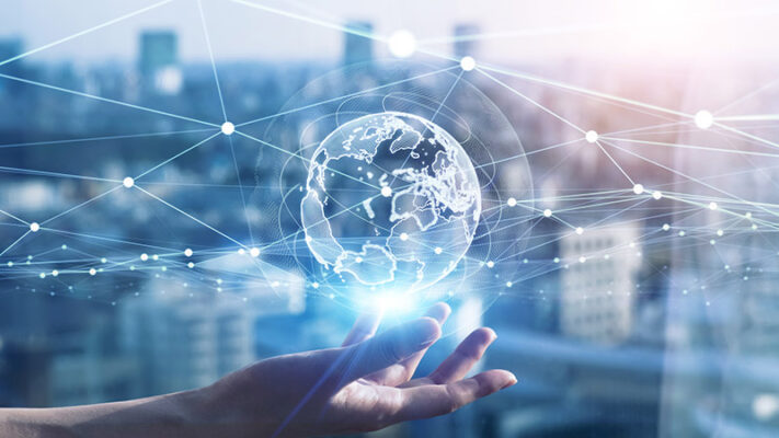 A hand holds a translucent digital globe with interconnected lines set against a blurred cityscape background.