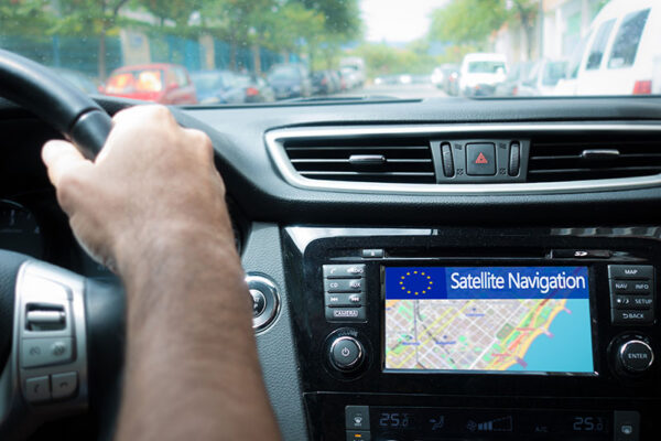 A person driving a car with a GPS navigation system displaying a map and the words "Satellite Navigation" on the screen.