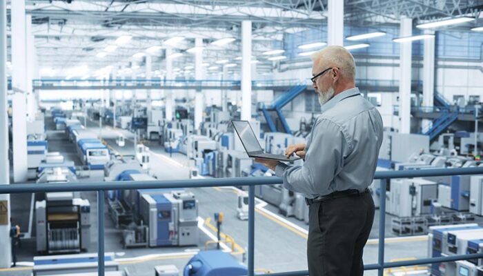 A person with a laptop observing a factory floor, monitoring machinery and equipment through real-time IIoT data.