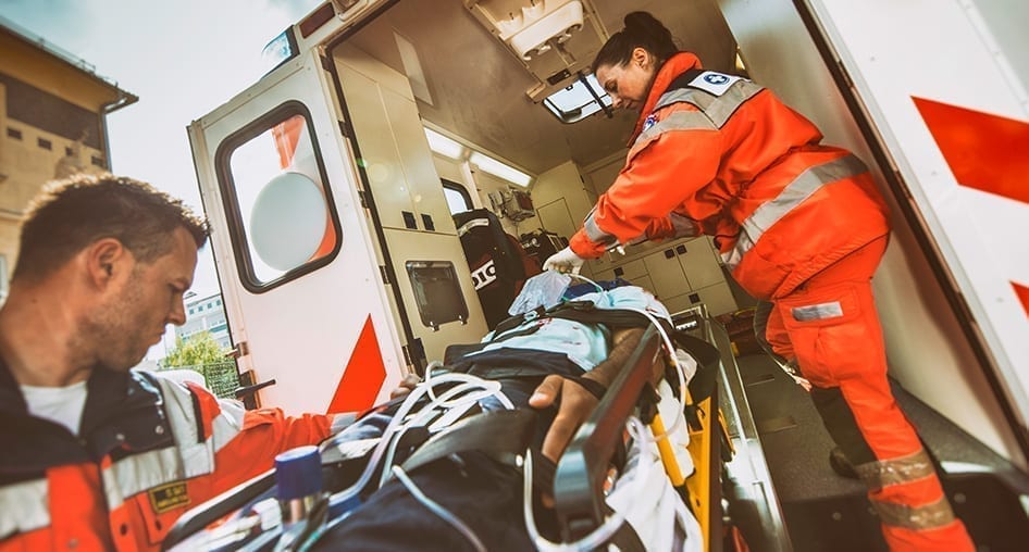 Two first responders loading a patient in a gurney onto an ambulance.