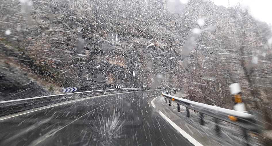 Snow hitting a windshield while driving fast on a winding road.