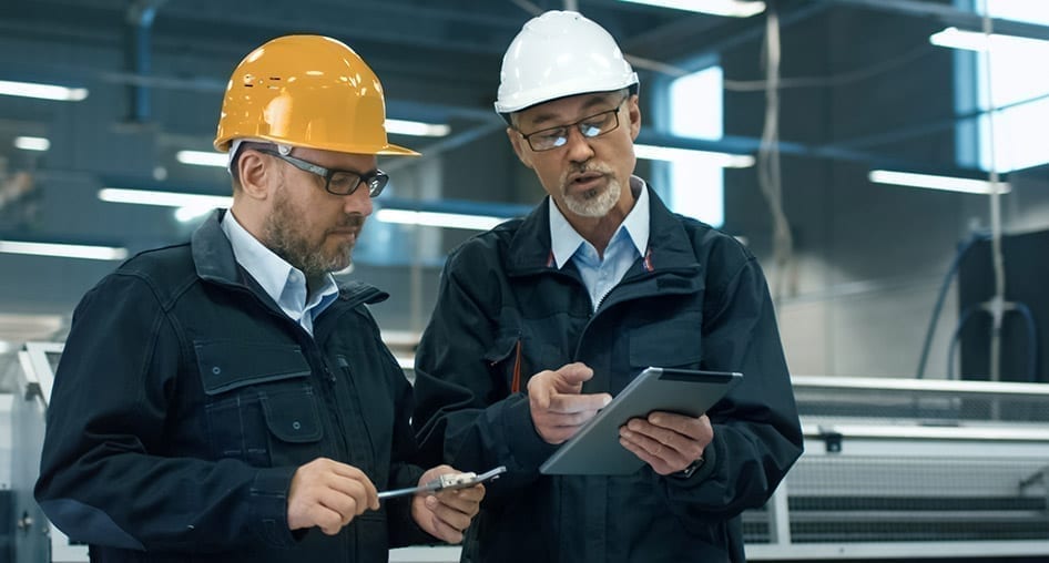 Two people in a factory wearing hardhats and looking at data on a tablet.