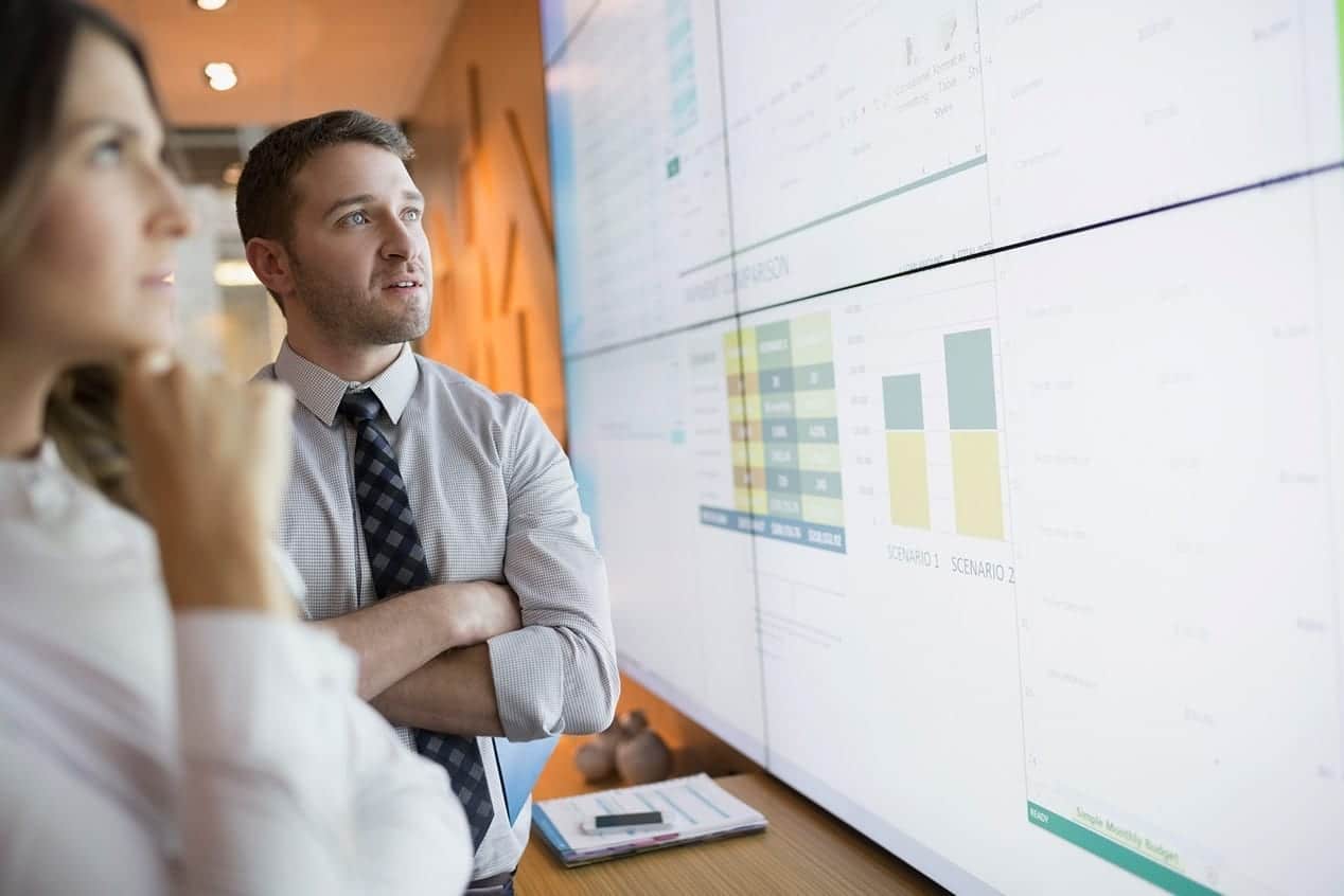 Two people analyzing data on a large monitor.