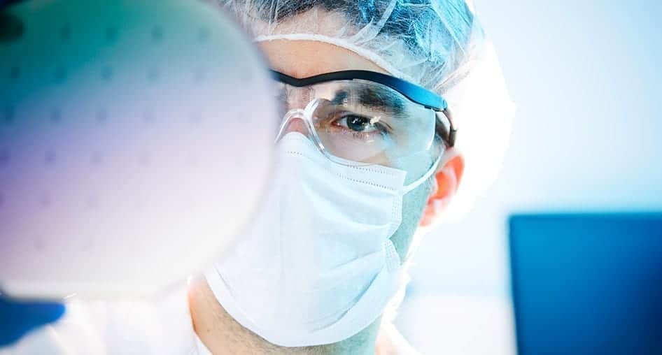 Extreme close-up portrait of a person wearing surgical mask and a hair net focused on their work.