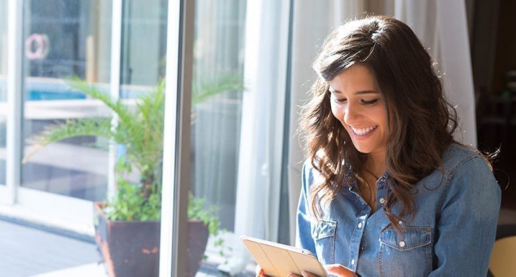 A happy person by a window looking at a tablet.