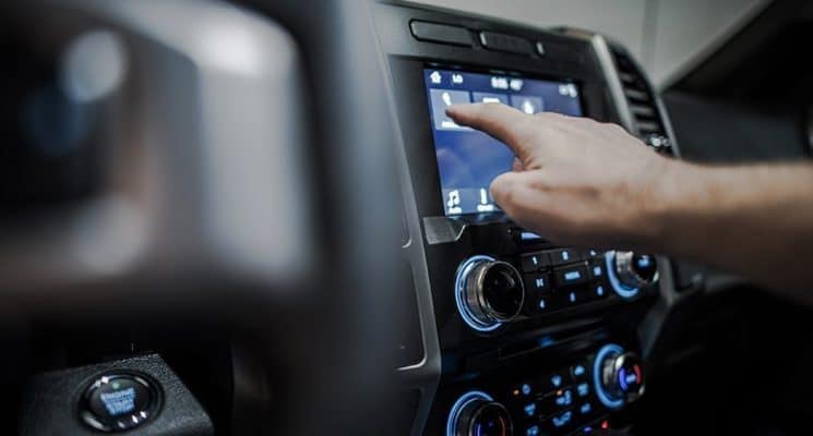 Person tapping a button on a touch screen on the dashboard of their vehicle.