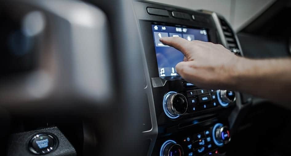 Person tapping a button on a touch screen on the dashboard of their vehicle.