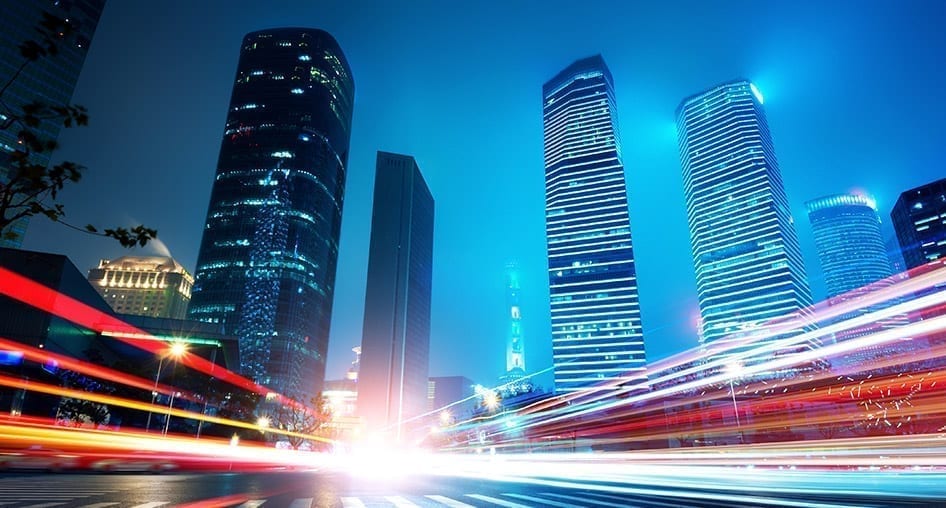 Street view of a city at night at a crosswalk. Motion blur from headlights and tail lights on both sides of the crosswalk.