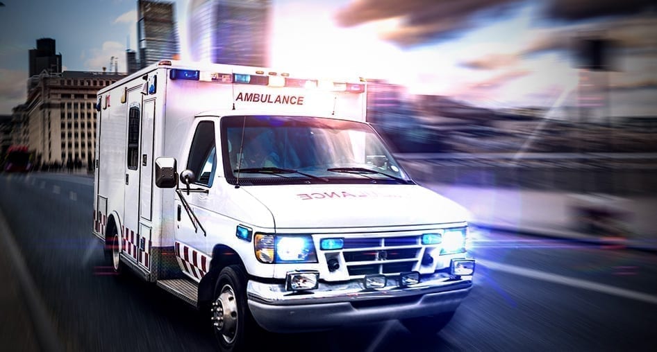 An ambulance with its lights on speeding down the highway in a city.
