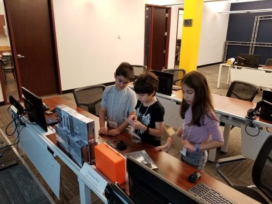 A group of kids working on computers in an office.