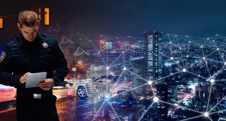 Merged image of a first responder adding information to a tablet next to an aerial view of a city at night with a network of connected dots.