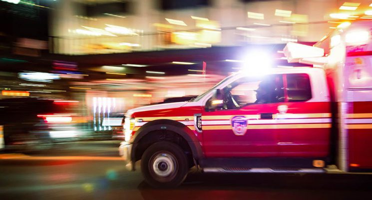 An ambulance with lights on, speeding through a city.