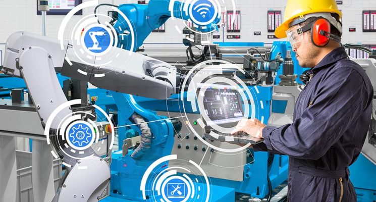 Factory worker wearing a hard hat, ear protection and safety goggles, controlling robotic arms with a laptop. The image is overlaid with icons for connectivity and smart manufacturing.