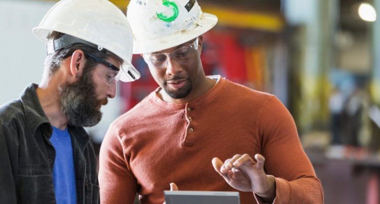 Two people in hardhats looking at a tablet.