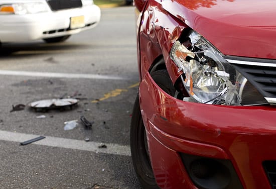 A headlight of a vehicle broken after a minor accident, with car debris on the pavement and a police car in the background.
