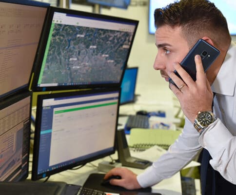 A man talking on a cell phone in front of several monitors.