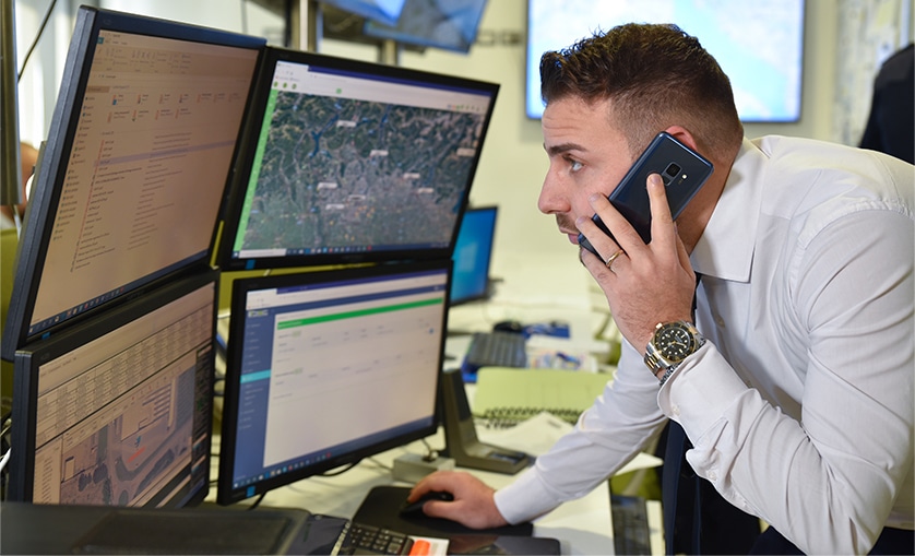 A man talking on a cell phone in front of several monitors.