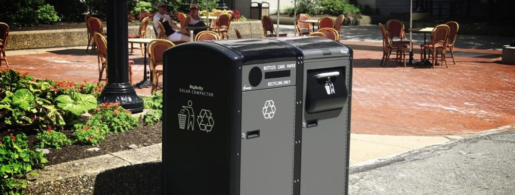 A black and gray trash receptacle sits on a sidewalk.