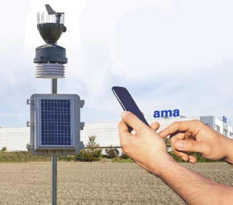 A person holding a cell phone next to a solar powered weather station.