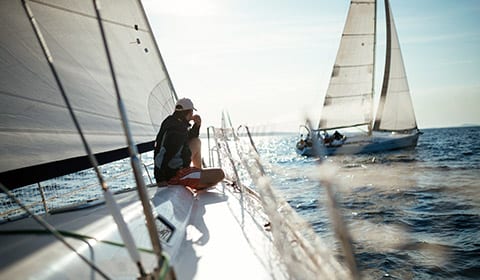 Two people sitting on a sailboat in the ocean.