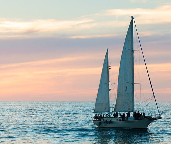 A sailboat sails in the ocean at sunset.