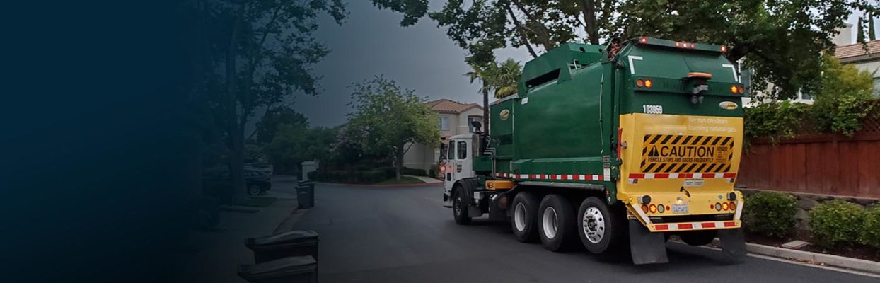 A green garbage truck driving down a residential street.