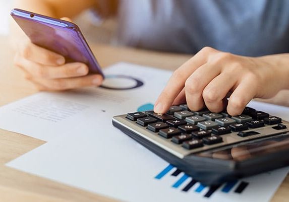 A person is using a calculator while holding a cell phone for IoT asset tracking purposes.