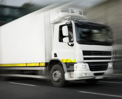 A white truck driving down the road with blurred motion.