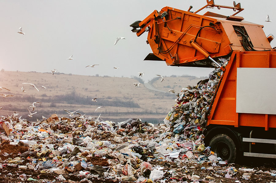 A trash collecting truck emptying waste in a landfill. Cities can leverage smart waste management solutions enabled with IoT to overcome waste management challenges.