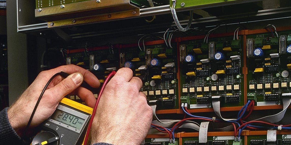 A man conducting maintenance on a machine with a multimeter as part of facilities management.