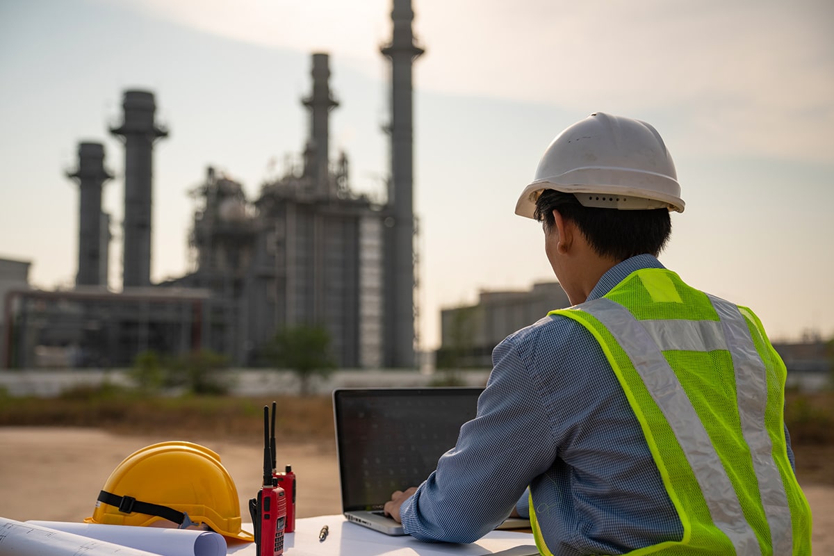 A man working on a laptop in front of an oil refinery uses deviceWISE CLOUD technology.