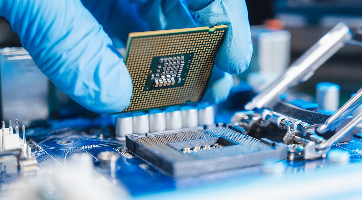 A person is holding a CPU on top of a motherboard, showcasing the use of remote connectivity in IIoT platforms for semiconductors.