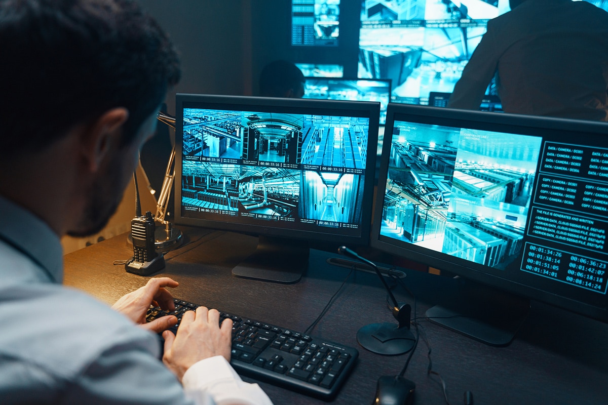 A person watching live security and surveillance footage on multiple screens.