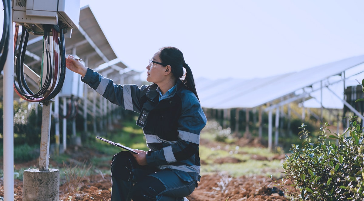 A woman inspecting a solar panel in a field, harnessing smart energy for IoT utilities.