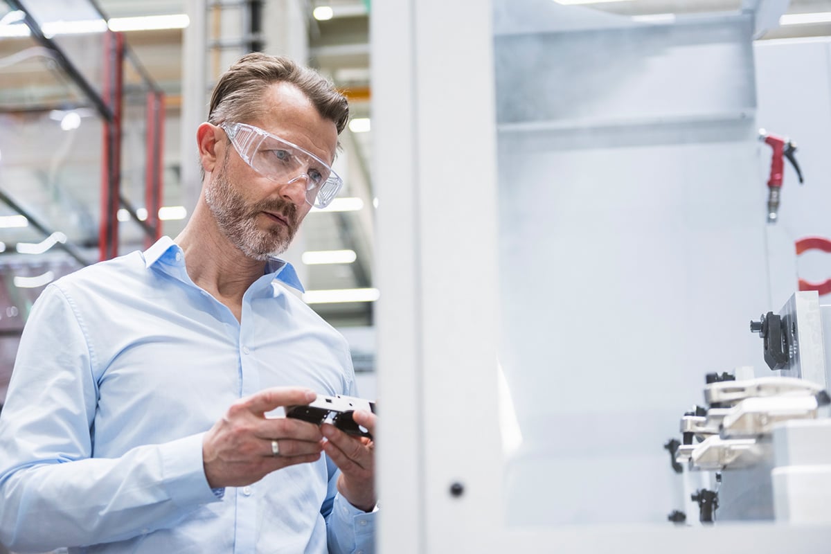 In a smart manufacturing environment, a man wearing safety goggles inspects a machine.