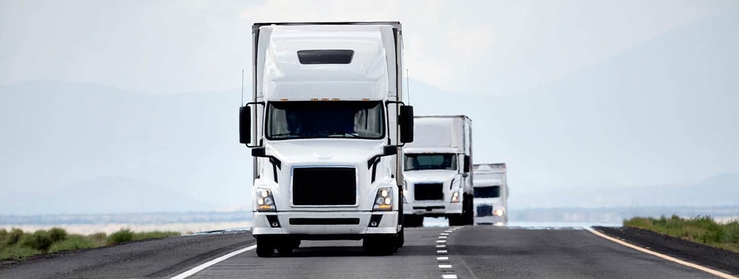 A fleet of white semi trucks driving on a road.