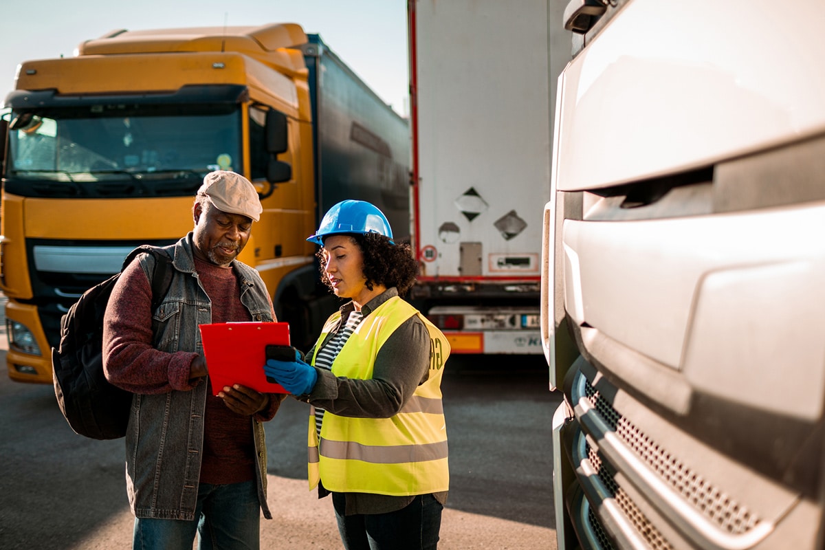 Two people examining a document in front of a truck used for transport.