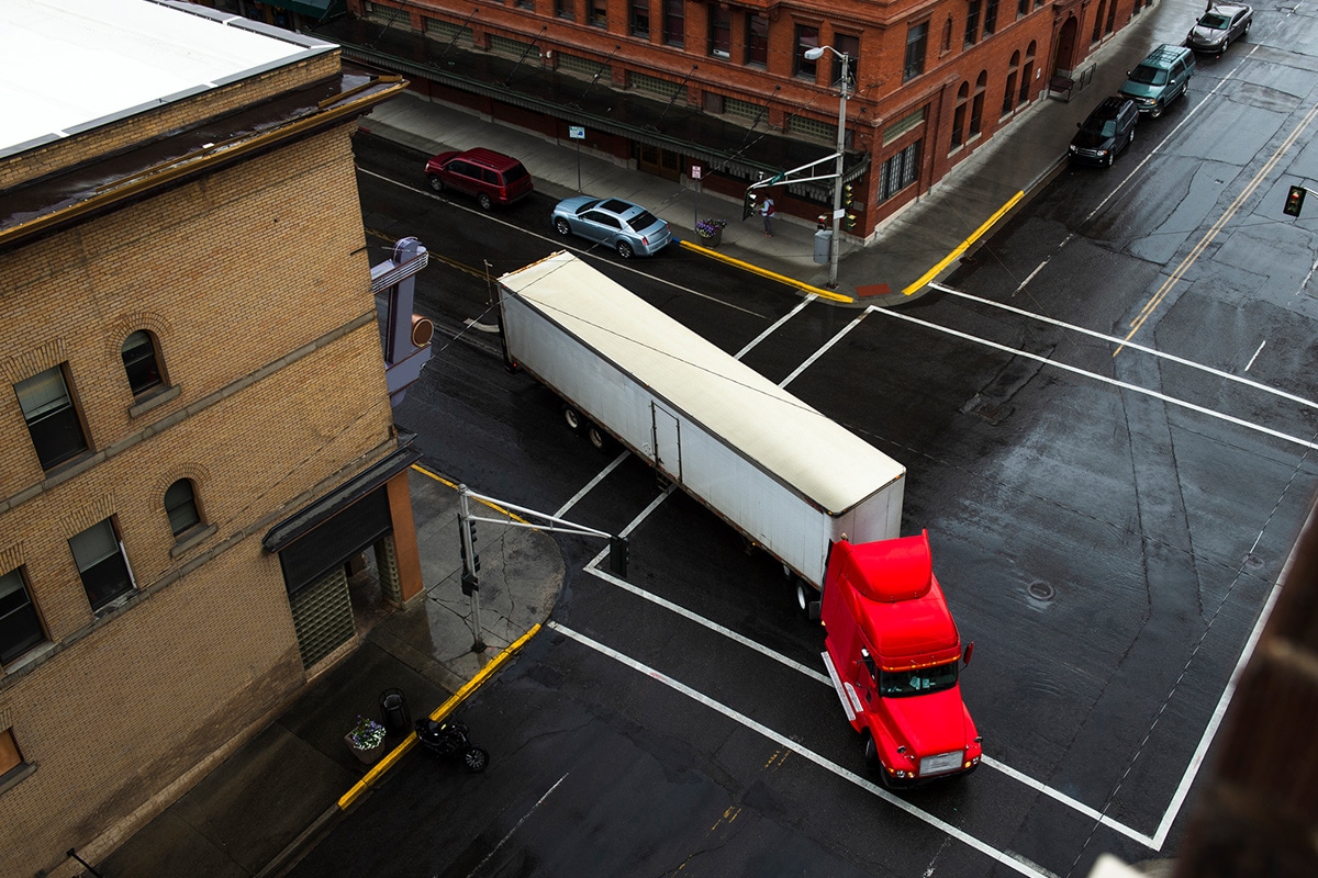 A red semi truck equipped with telematics technology driving through the city.