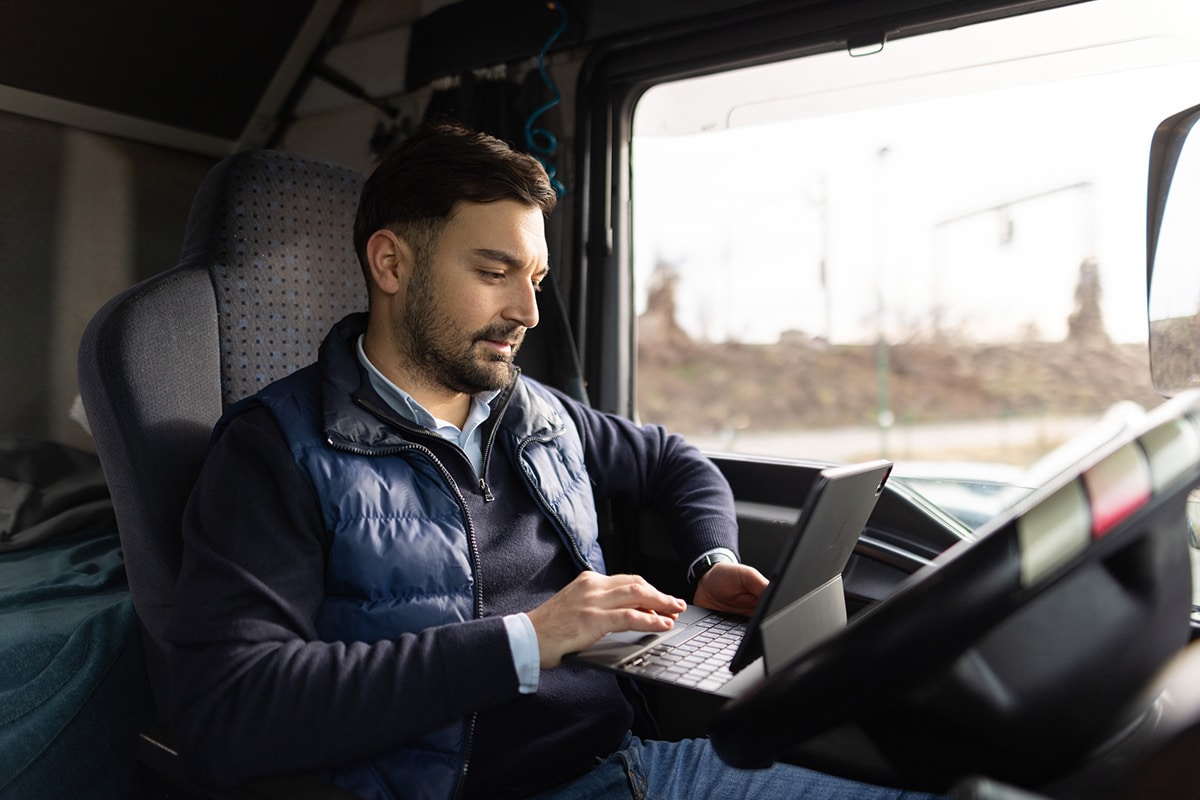 A man in the driver's seat of a truck using a laptop for telematics.