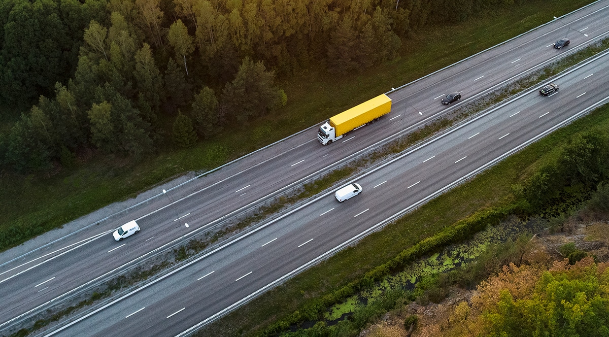 An aerial view of a yellow truck driving down a highway, showcasing advanced telematics technology in transport.